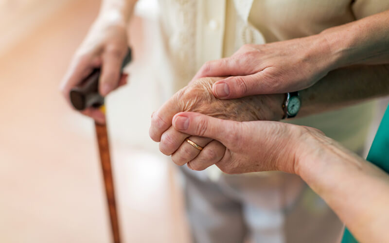 Nurse helping elderly person with Parkinson’s walk using a cane