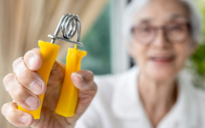 Elderly Asian woman holding medical device to strengthen hand as a form of Parkinson’s treatment
