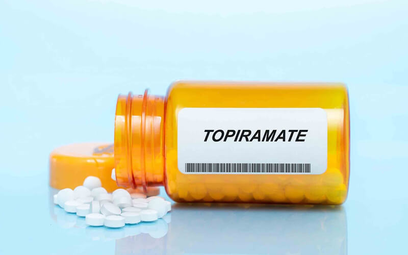 Bottle of Topiramate on its side spilling out onto blue backdrop