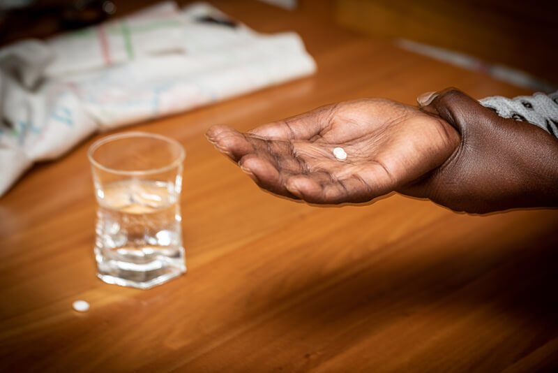 Photo of elderly Black womans hands shaking struggling to take medication