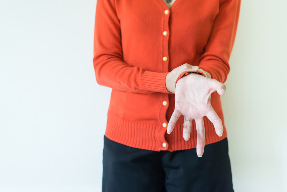 Senior woman in red sweater experiencing hand tremors due to Parkinson’s disease