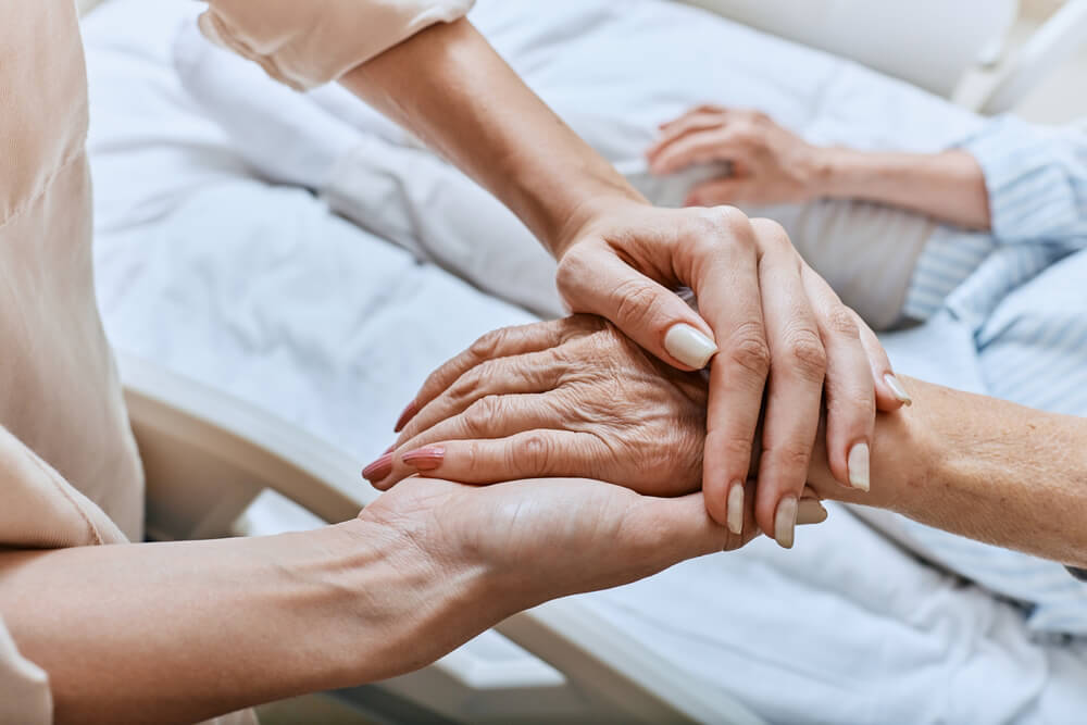 Young person’s hands holding elderly Parkinson’s patient’s hands