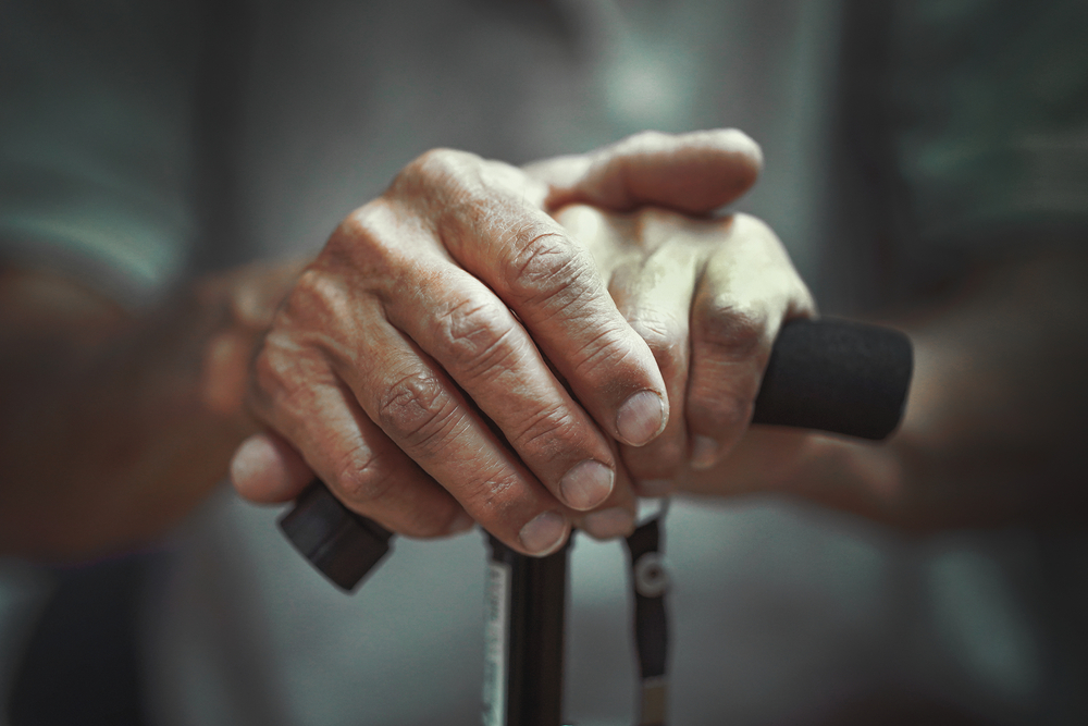 Close-up of old person’s hand holding a cane